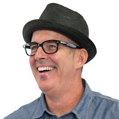 Headshot of a man with thick black glasses and wearing a black fedora
