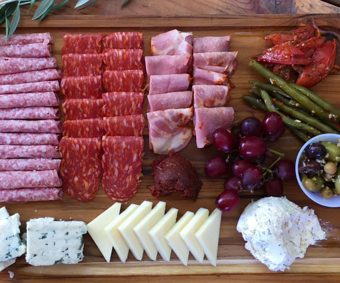 Cured meats and cheeses are laid out on a wooden charcuterie board in Mesa, Arizona.
