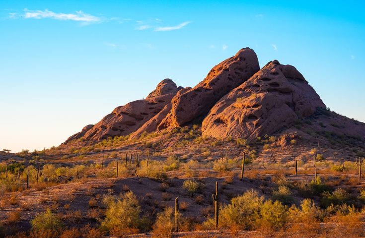 Red mountain formation off Papago Park hiking trail against clear blue skies with wispy clouds.