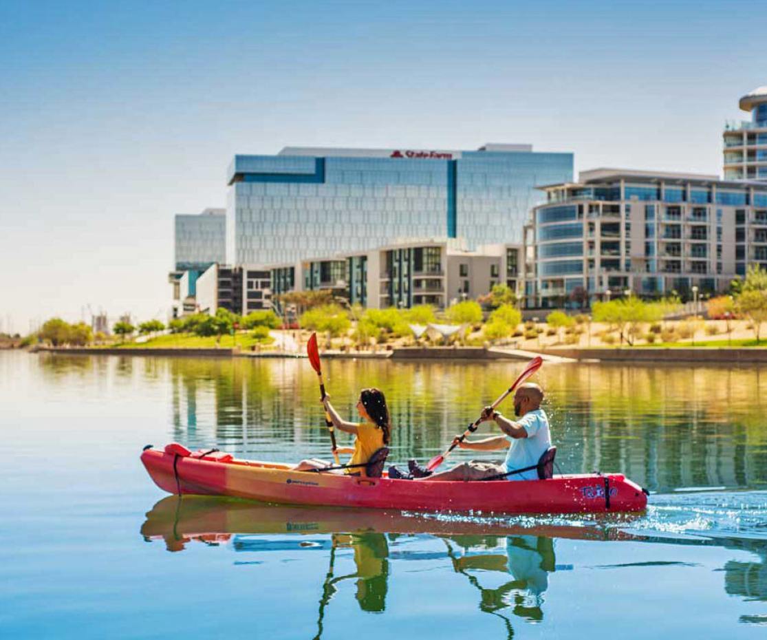 A double kayak containing two passengers makes its way down Tempe Town Lake with Tempe, Arizona in the background.
